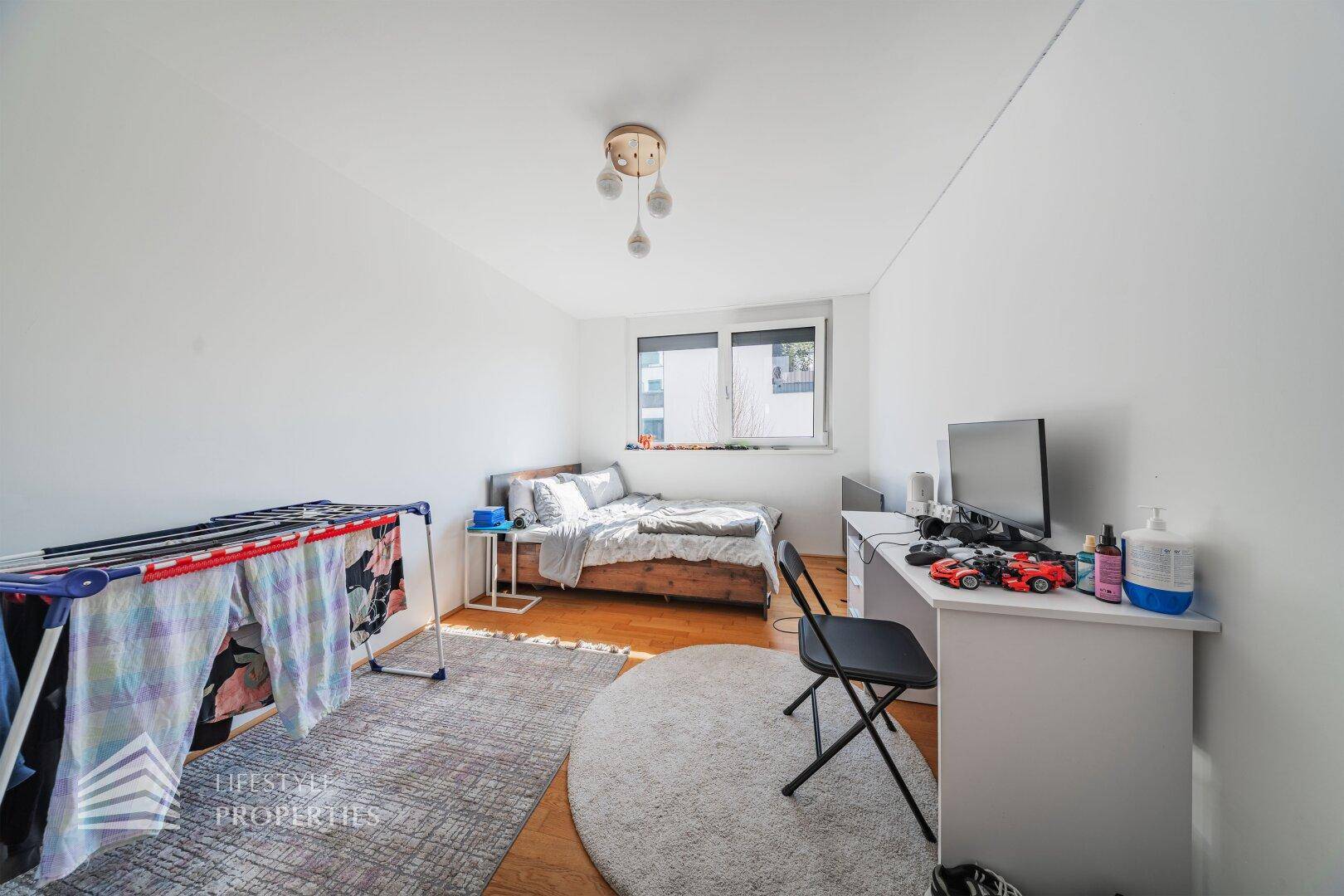 Helles Schlafzimmer, das als Büro genutzt wird, mit Holzboden, Bett und Schreibtisch am Fenster.