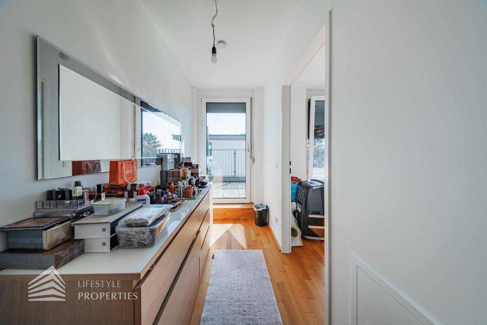 Heller Flur oder Ankleidebereich mit großem Spiegel, Kommode und Zugang zu einem Balkon.