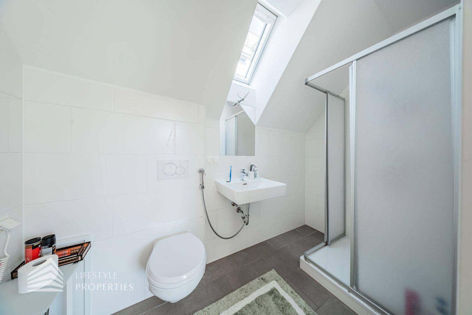 Modernes Badezimmer mit Duschkabine, Toilette, Waschbecken und einem Dachfenster für Tageslicht.