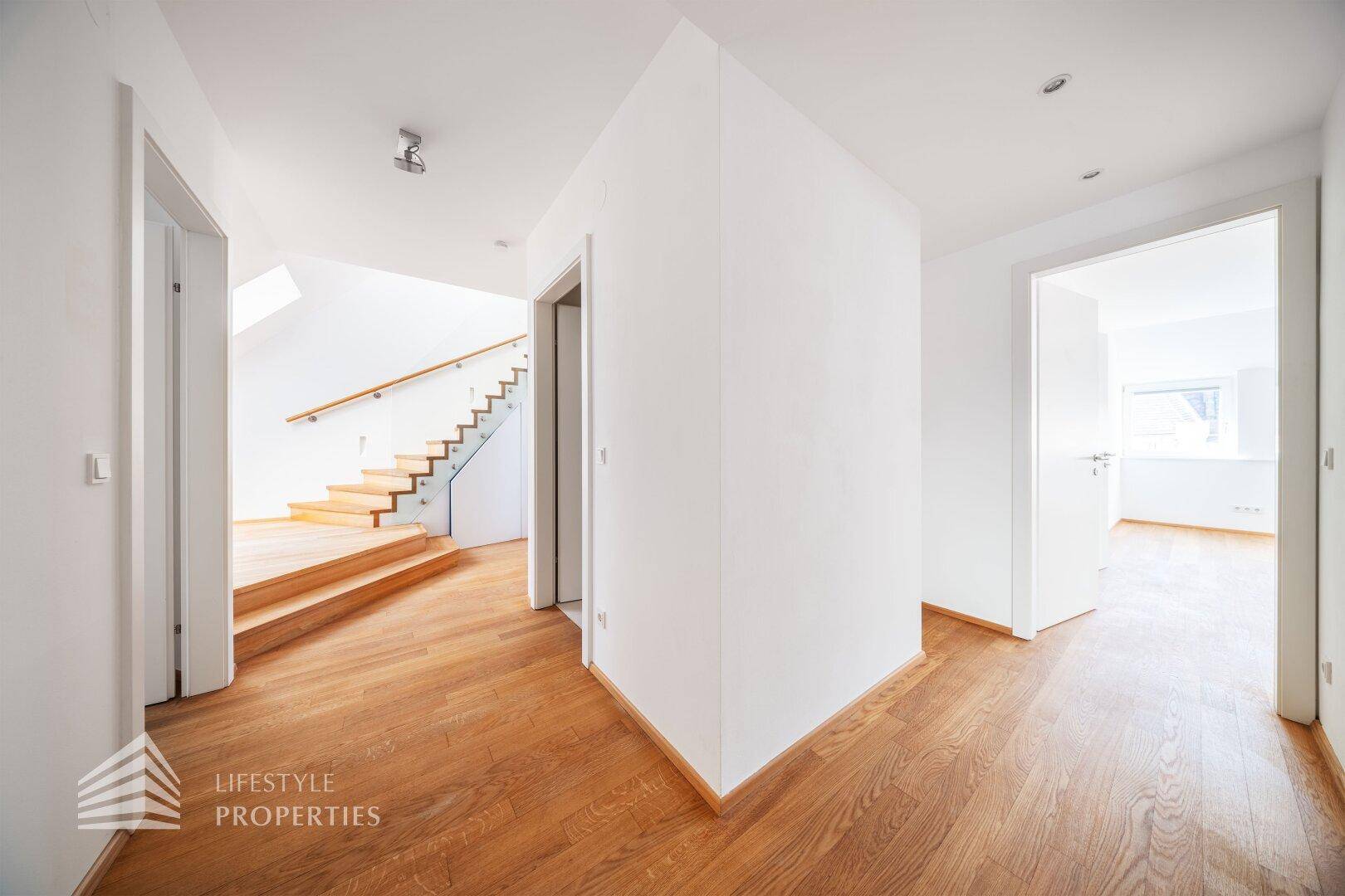 Heller Flur mit Holzboden und moderner Holztreppe mit Glasgeländer.