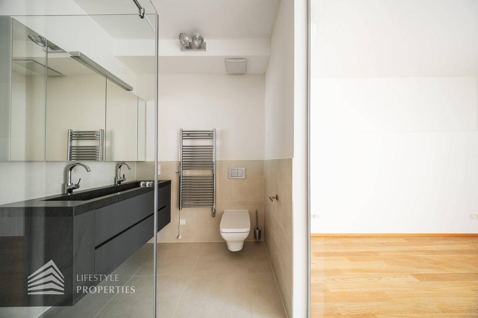 Modernes Badezimmer mit Doppelwaschbecken, Dusche, Toilette und beheiztem Handtuchhalter.