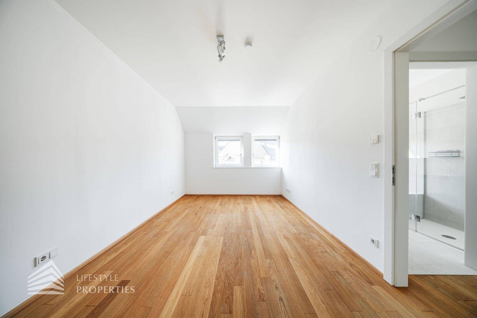 Helles Schlafzimmer mit Holzboden, weißen Wänden und zwei Fenstern.