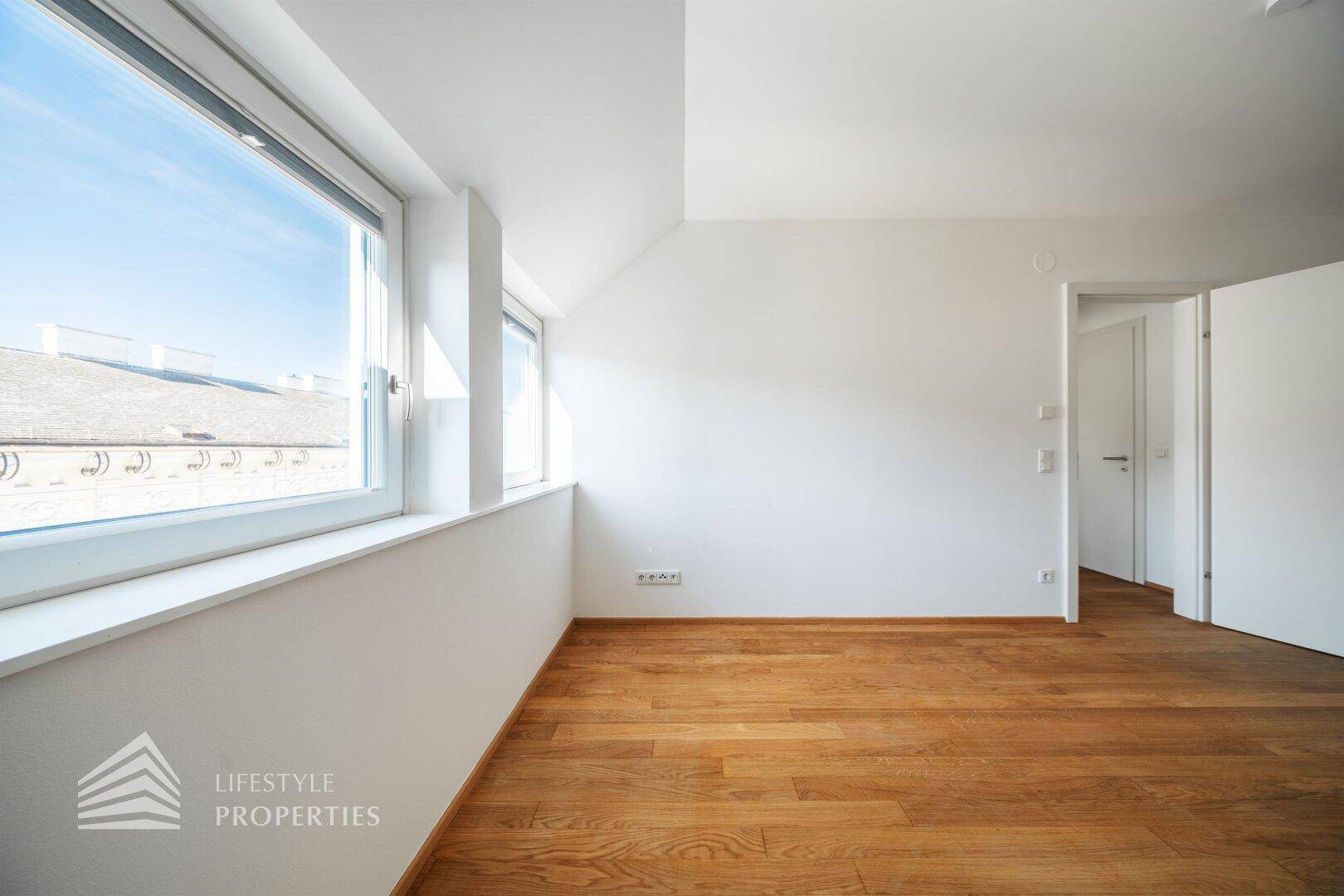 Geräumiges Schlafzimmer mit Holzboden, großen Fenstern und Blick auf die Stadt.