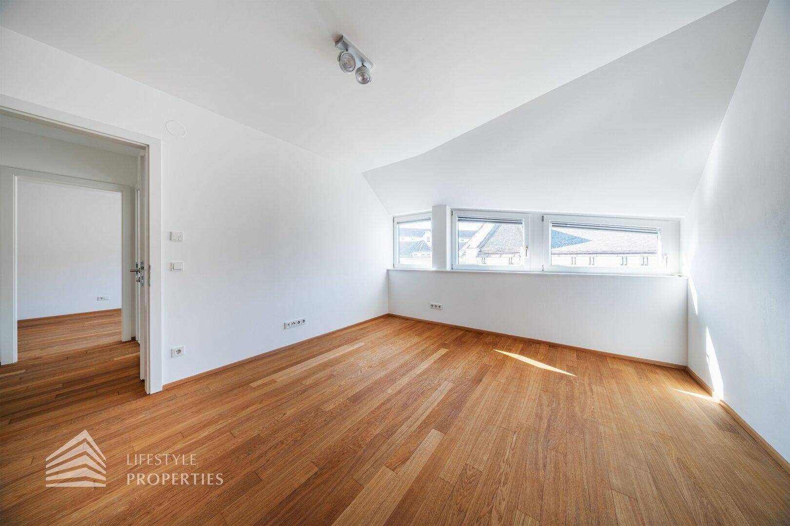 Helles Schlafzimmer mit Holzboden, weißen Wänden und breiten Fenstern.