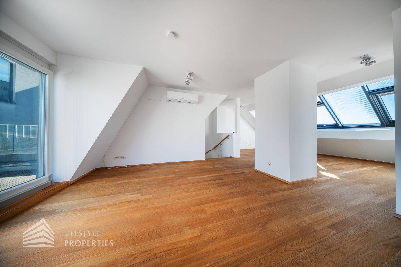Offener Wohnbereich mit Holzboden, Klimaanlage, Dachfenstern und Terrassenzugang.