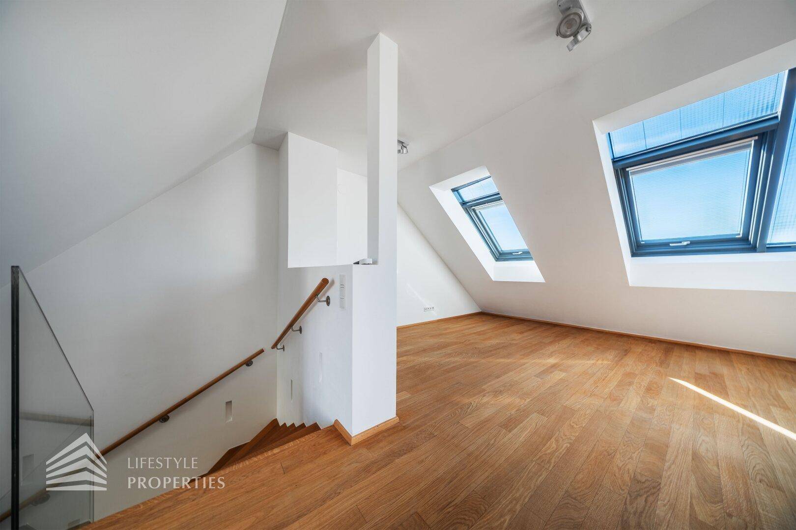 Heller Flurbereich mit Holztreppe, Glasgeländer und Dachfenstern.