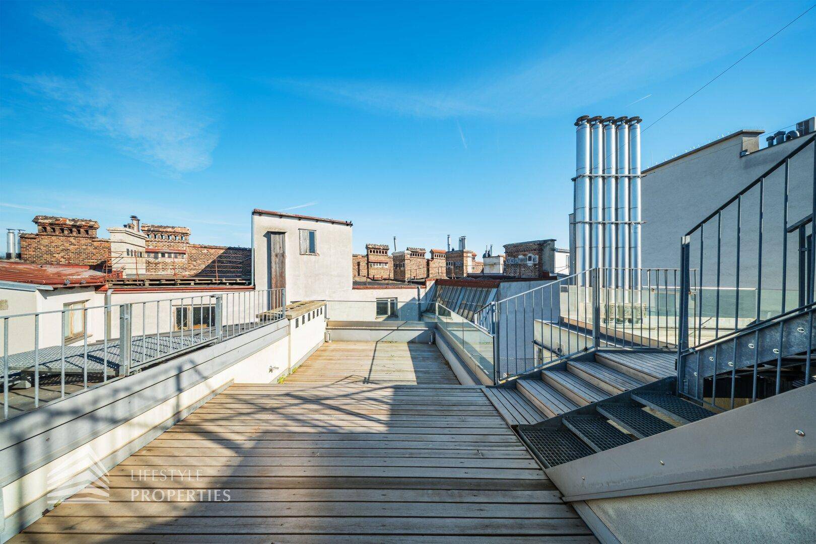 Weitläufige Dachterrasse mit Holzplanken und Blick über die umliegenden Dächer der Stadt.