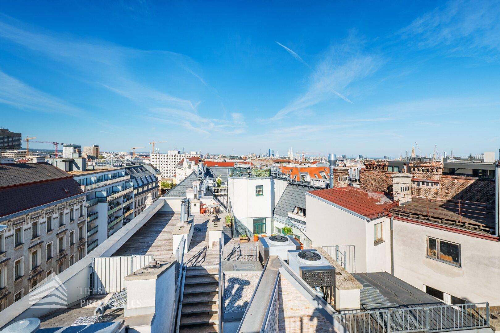Ausblick über die Dächer der Stadt mit verschiedenen Gebäudetypen und weitem Horizont.