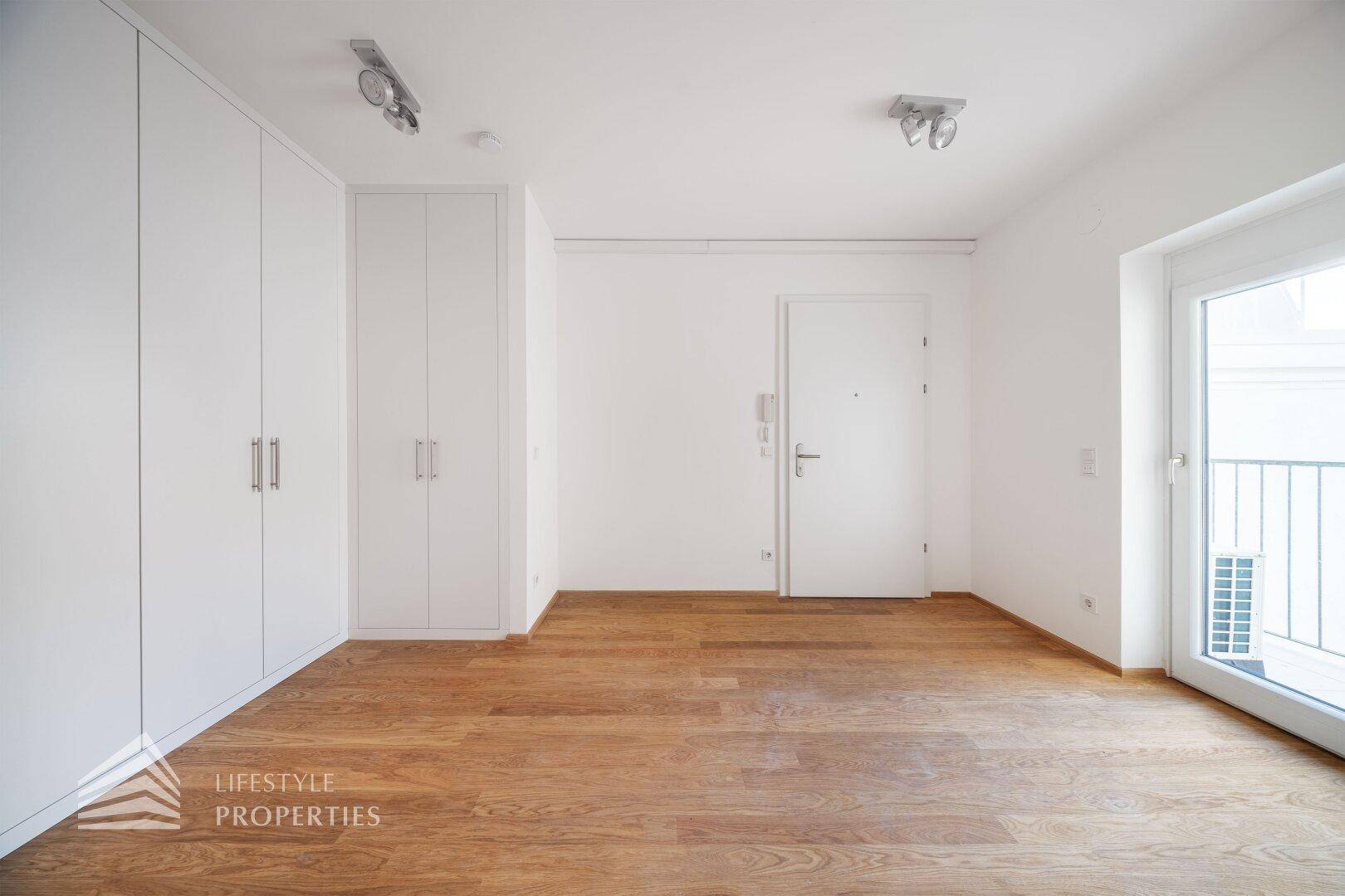 Eingangsbereich mit Holzboden, weißen Einbauschränken und Zugang zur Wohnung.
