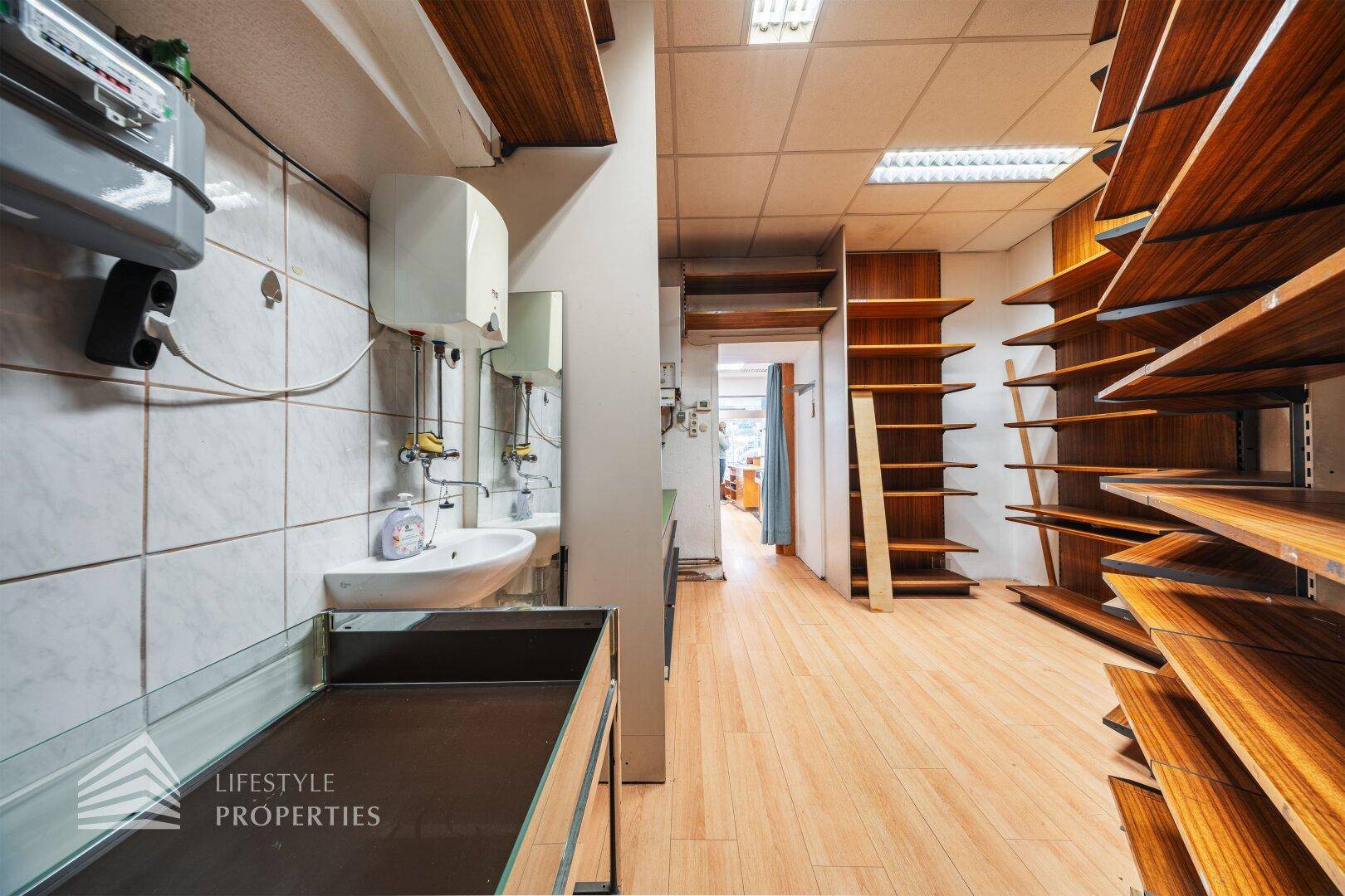 Kleiner Hauswirtschaftsraum mit Waschbecken und gefliesten Wänden, führt zu weiteren Lagerräumen.