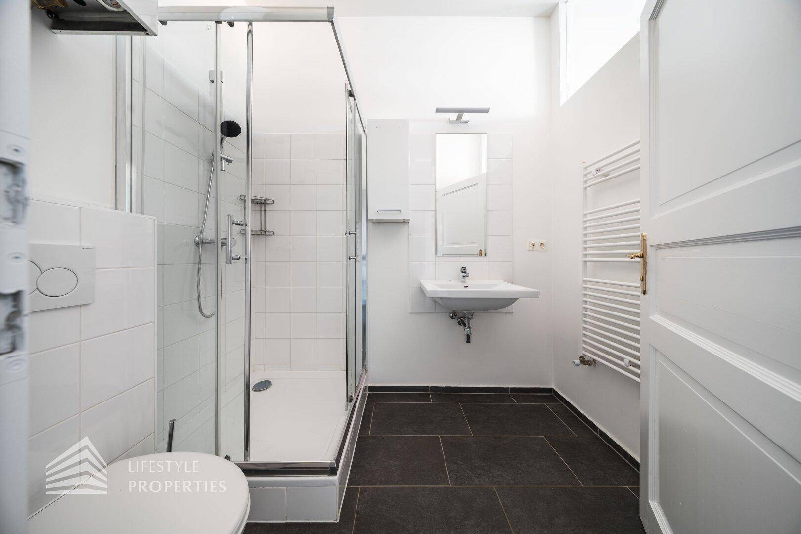 Modernes Badezimmer mit Duschkabine, wandhängendem WC, Waschbecken und beheiztem Handtuchhalter.