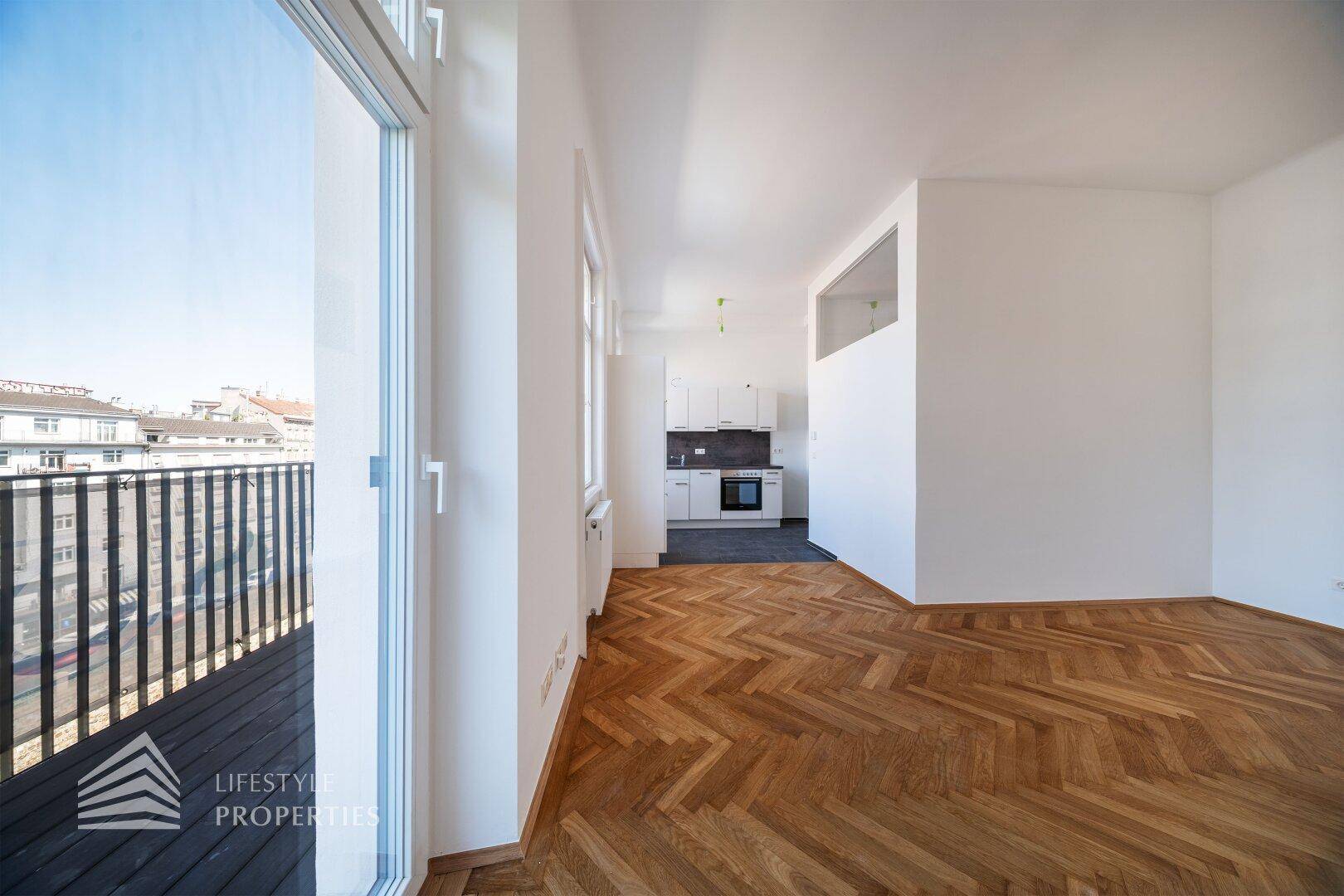 Lichtdurchfluteter Wohnbereich mit offener Küche, Fischgrätparkett und Zugang zu einem französischen Balkon.