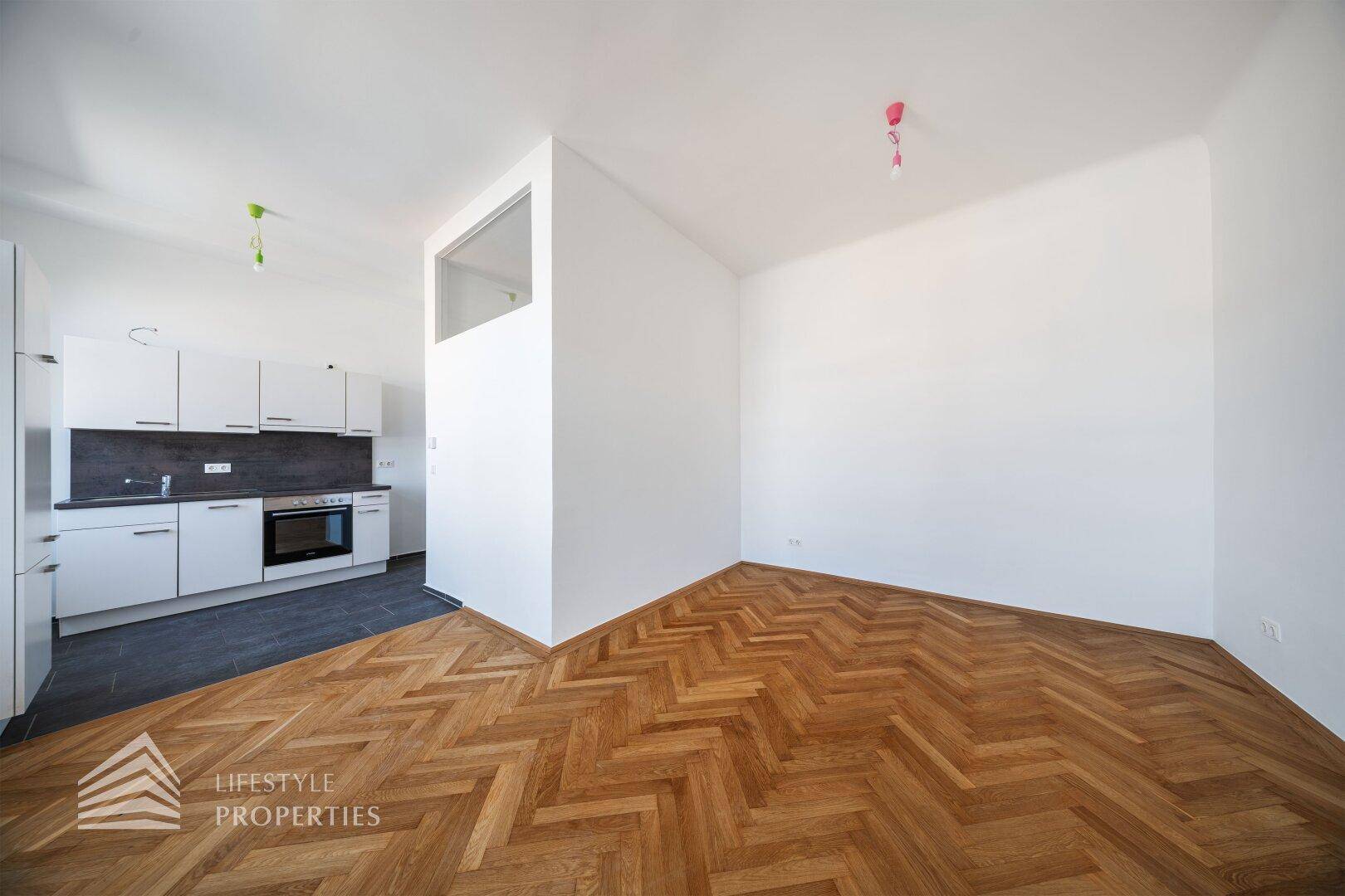 Heller Wohnbereich mit integrierter Küchenzeile und elegantem Fischgrätparkett, ideal für modernes Wohnen.