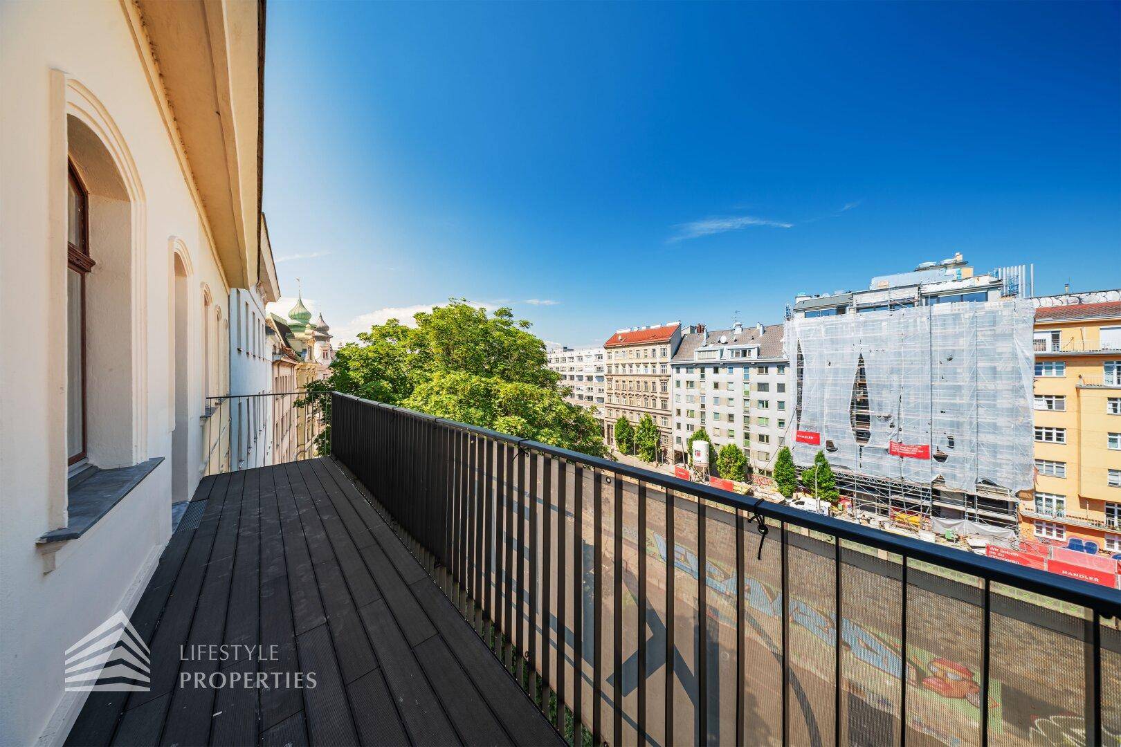 Langer Balkon mit Holzboden und Metallgeländer, bietet einen weiten Blick über die Stadt.