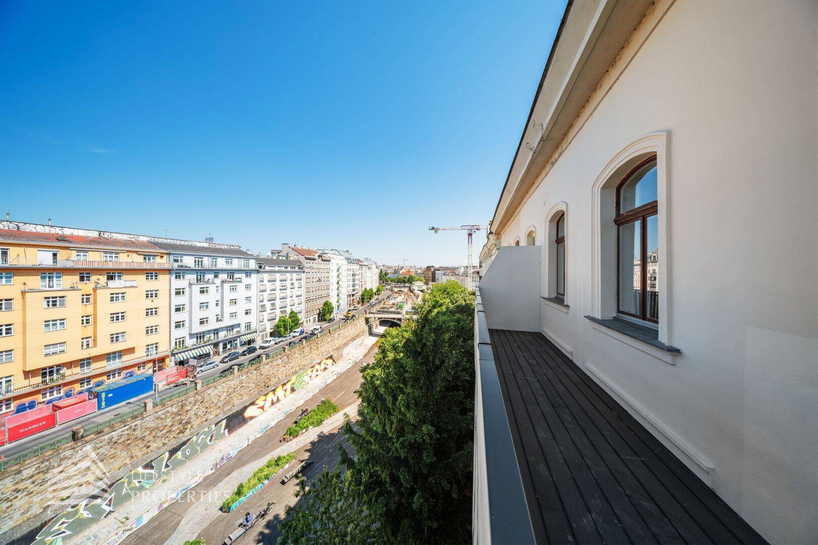 Geräumiger Balkon mit Holzboden und Blick auf die Stadt und die umliegenden Gebäude.