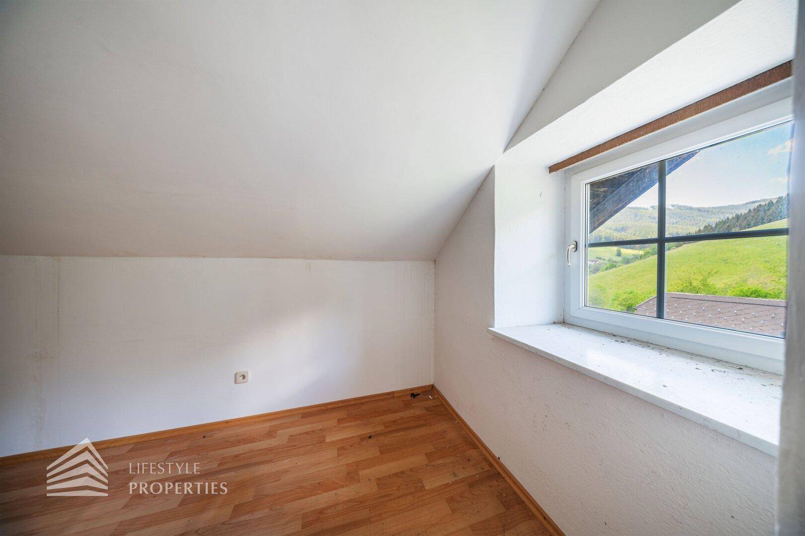 Gemütliches Schlafzimmer im Dachgeschoss mit Holzboden und Fenster mit Blick auf die Landschaft.