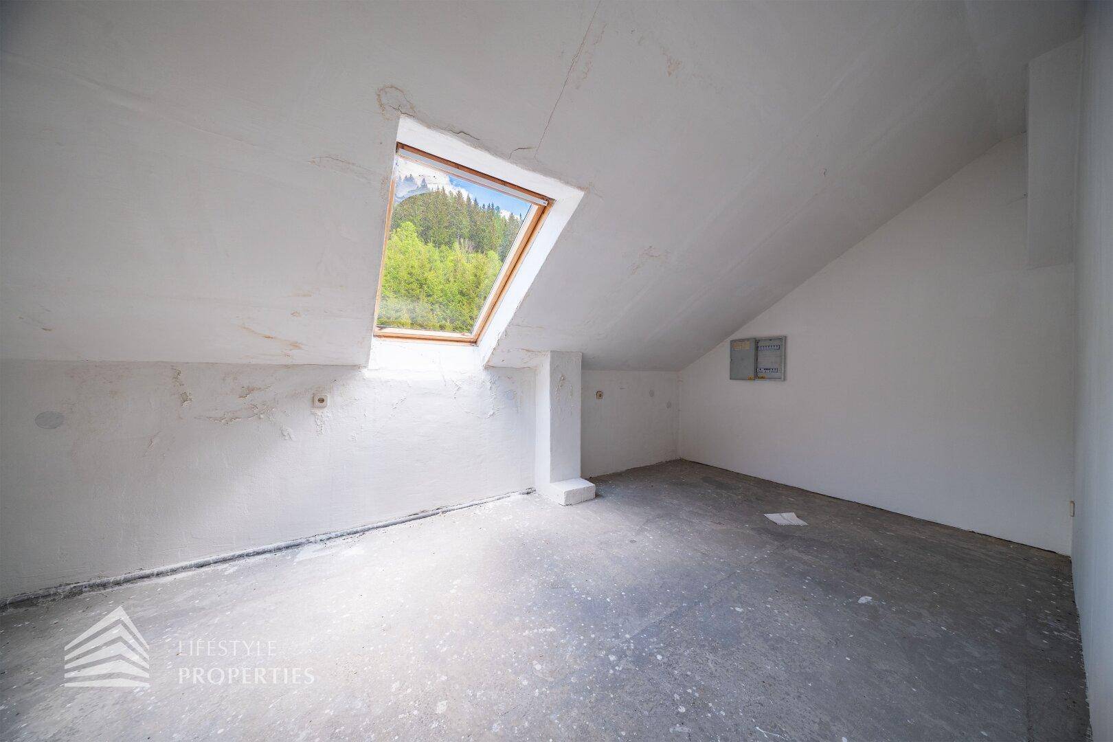 Unausgebauter Dachbodenraum mit großem Dachfenster und Blick ins Grüne.