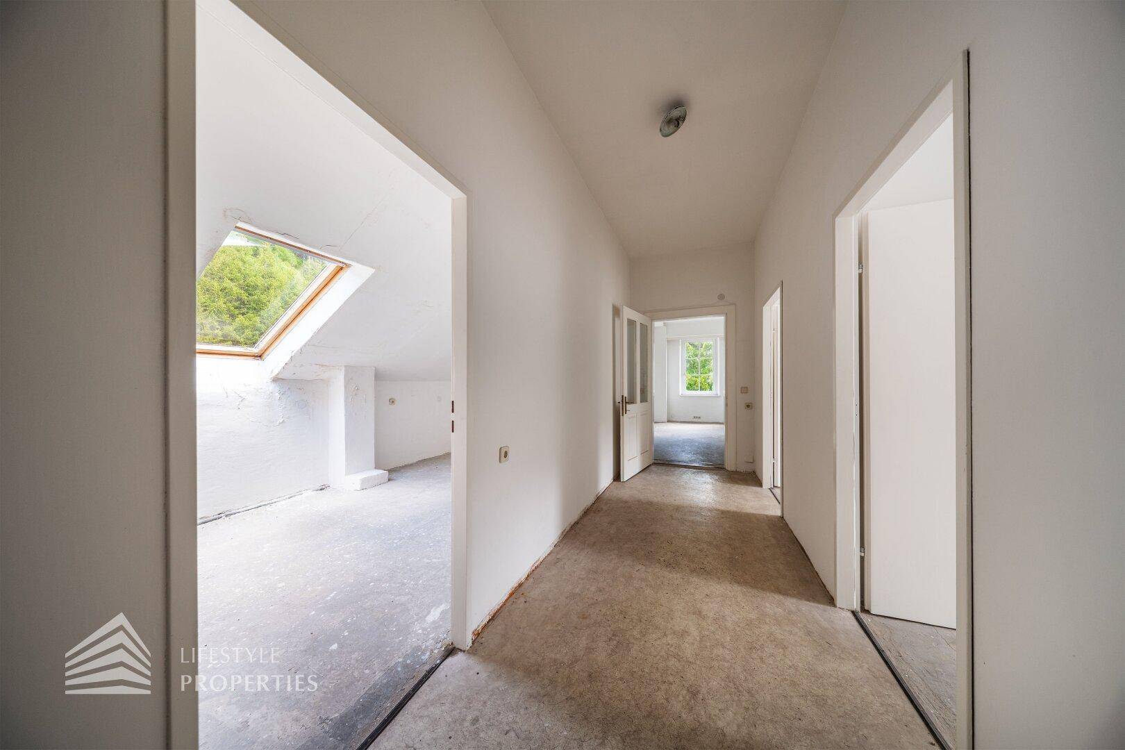Heller Flur mit Zugang zu mehreren Räumen und einem Dachfenster im angrenzenden Bereich.