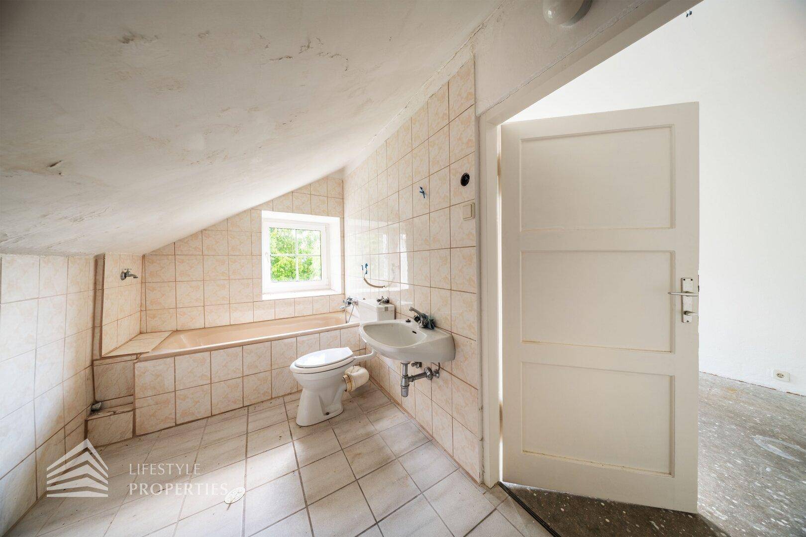 Gefliestes Badezimmer im Dachgeschoss mit Badewanne, WC, Waschbecken und Fenster.