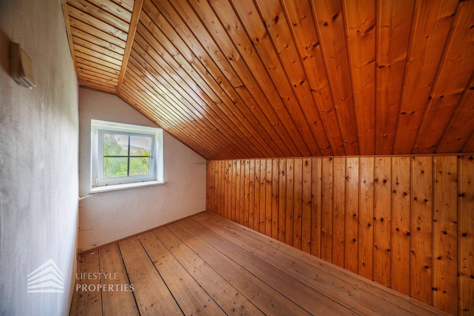 Gemütlicher Dachbodenraum mit Holzverkleidung an Wänden und Decke sowie kleinem Fenster.