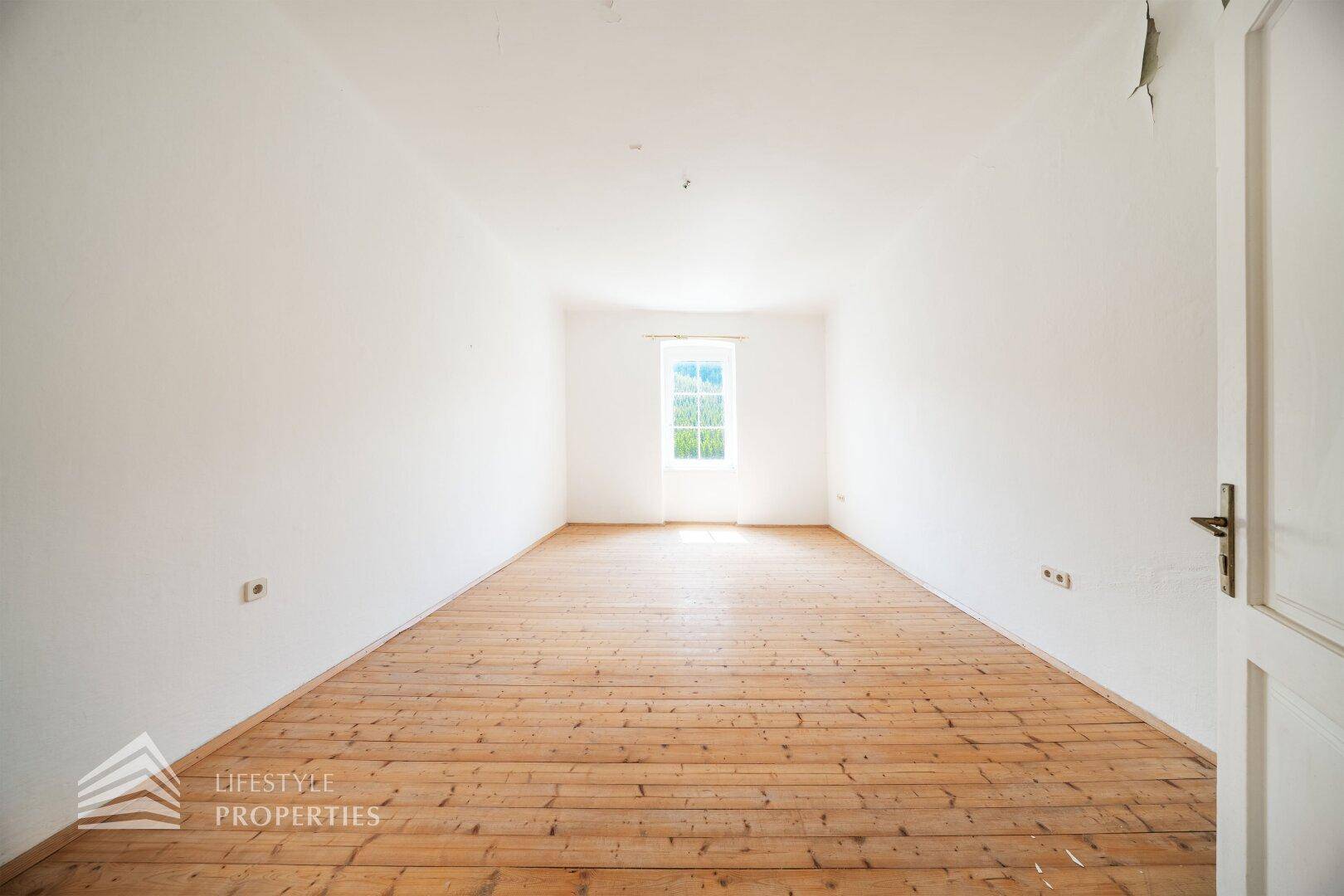 Langes, helles Wohnzimmer mit Holzdielenboden und einem Fenster am Ende des Raumes.