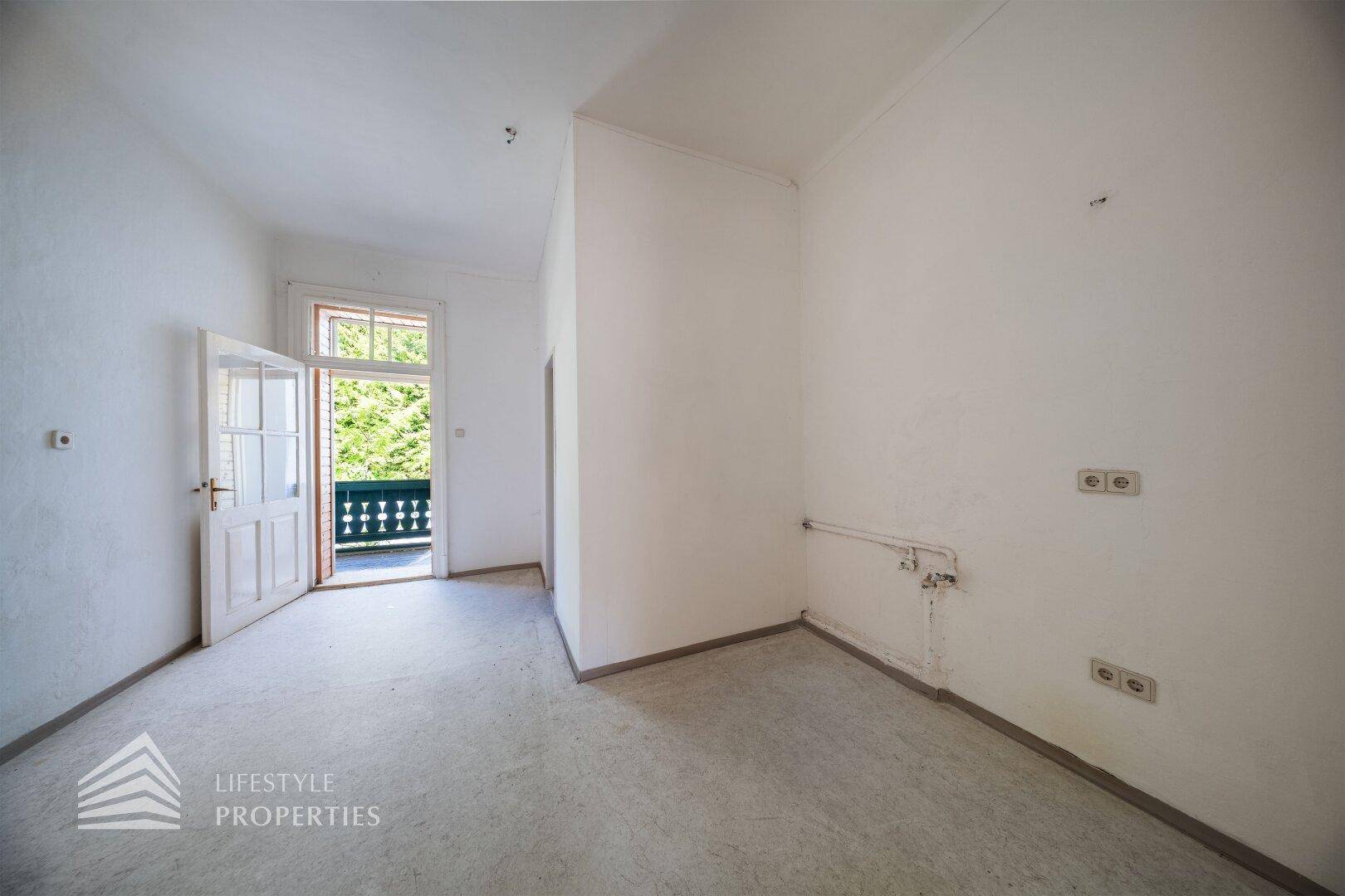 Leeres Zimmer mit Betonboden und Zugang zu einem Balkon mit Holzgeländer.