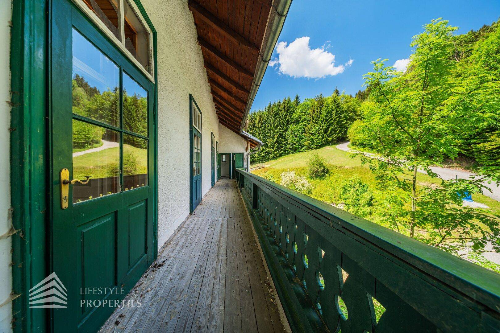 Langer Holzbalkon mit grünem Geländer und Blick auf die umliegenden Wälder.