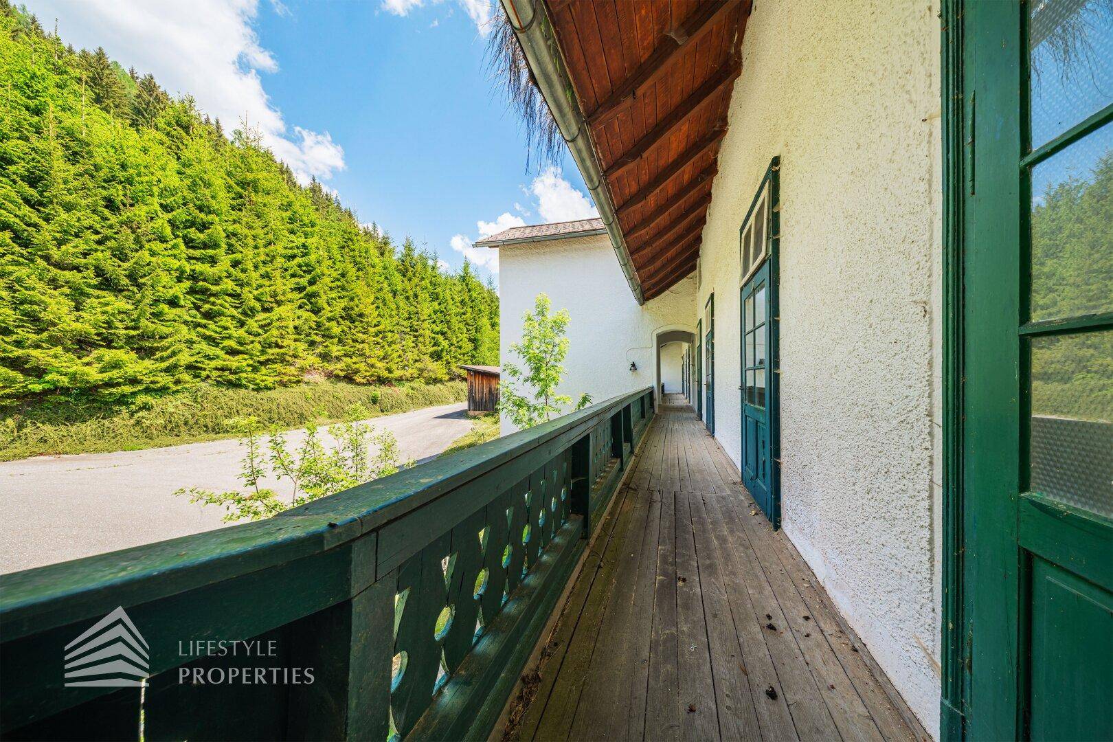 Geräumiger Holzbalkon mit traditionellem Geländer und Blick auf Wald und Straße.
