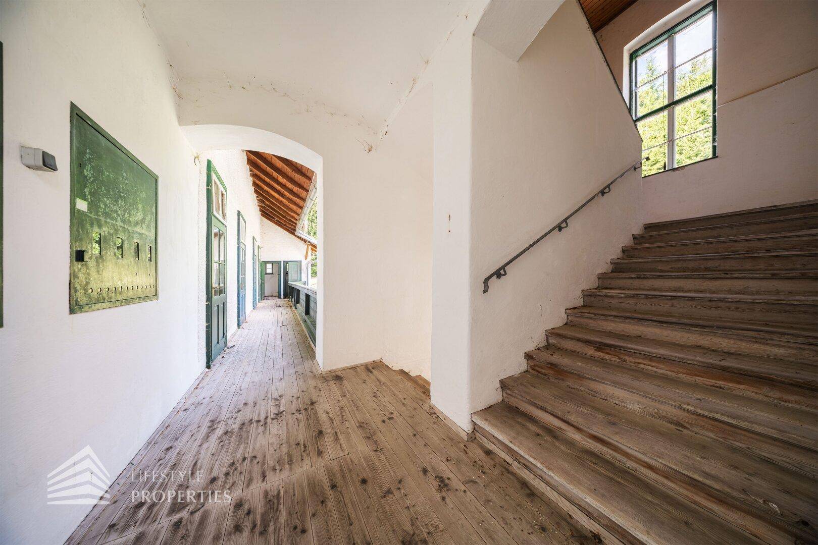 Helles Treppenhaus mit Holzdielenboden und Fenster, das viel Tageslicht hereinlässt.