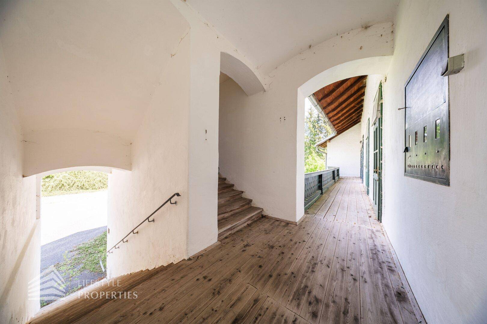 Flur mit Holzdielenboden, gewölbter Decke und Zugang zu einem langen Balkon.