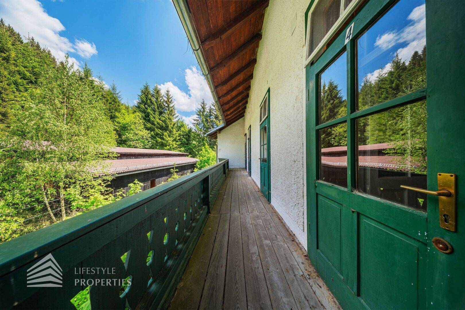 Langer Holzbalkon mit traditionellem Geländer und Blick auf die bewaldete Umgebung.