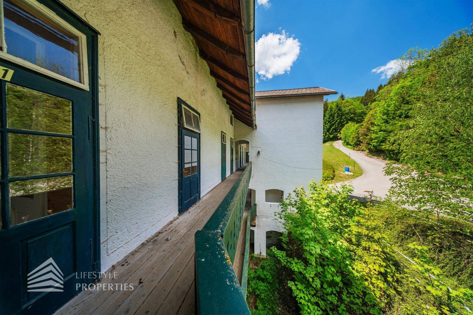 Geräumiger Holzbalkon mit traditionellem Geländer und Blick auf Wald und Straße.