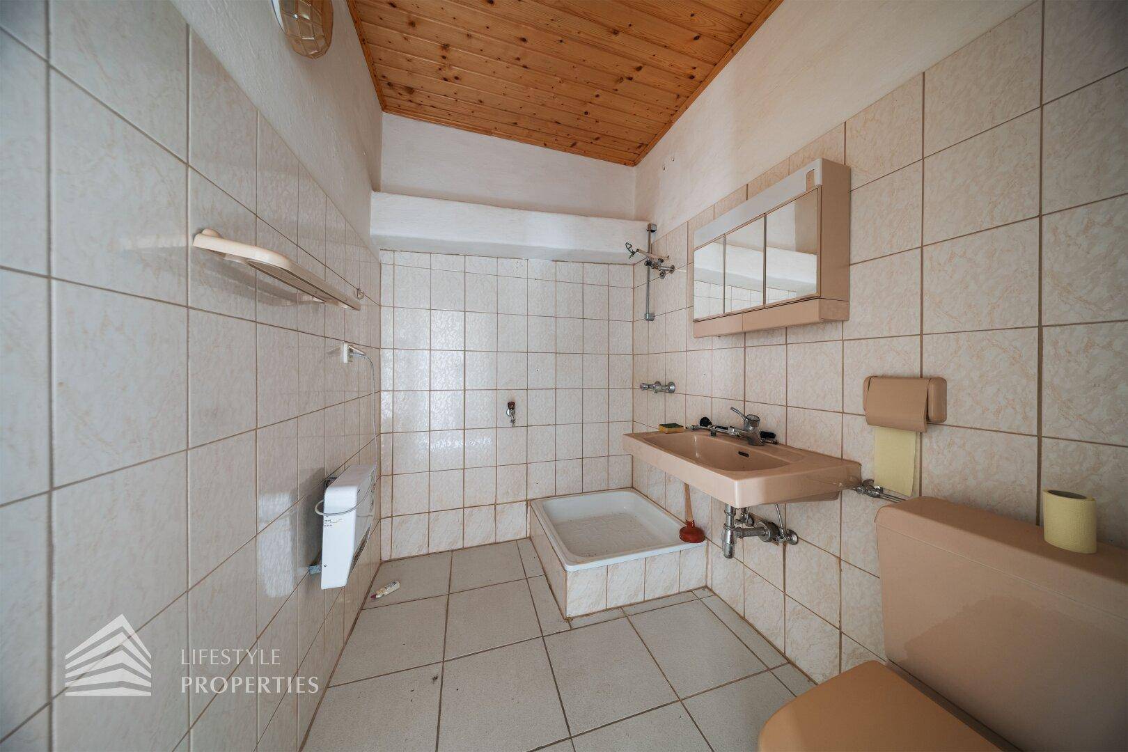 Gefliestes Badezimmer mit Dusche, Waschbecken, WC und Holzdecke im traditionellen Stil.