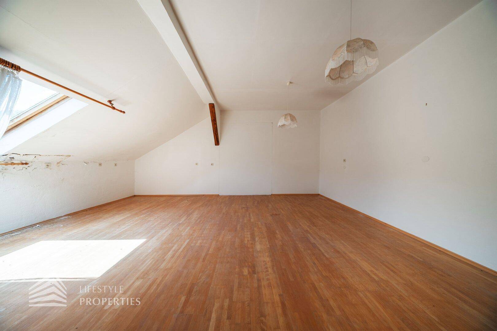 Geräumiger Dachraum mit Holzboden, schrägen Wänden und einem Dachfenster für natürliches Licht.