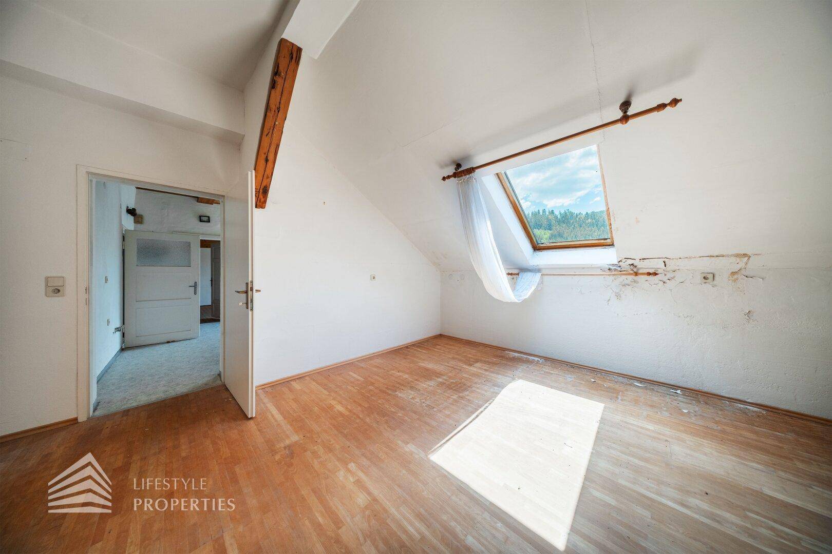 Lichtdurchfluteter Dachraum mit Holzboden, Dachfenster und einem Ausblick in die Natur.