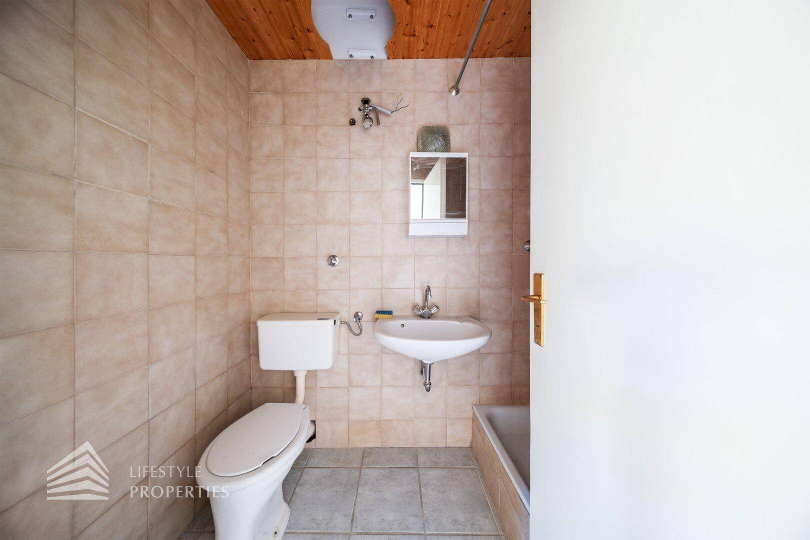 Funktionales Badezimmer mit beigefarbenen Fliesen, Toilette, Waschbecken und einer Badewanne.