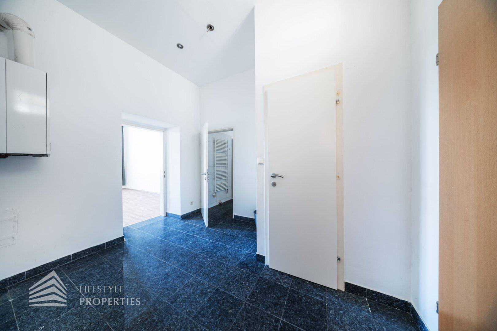 Flur mit dunklem Fliesenboden und Zugang zu verschiedenen Räumen der Wohnung.
