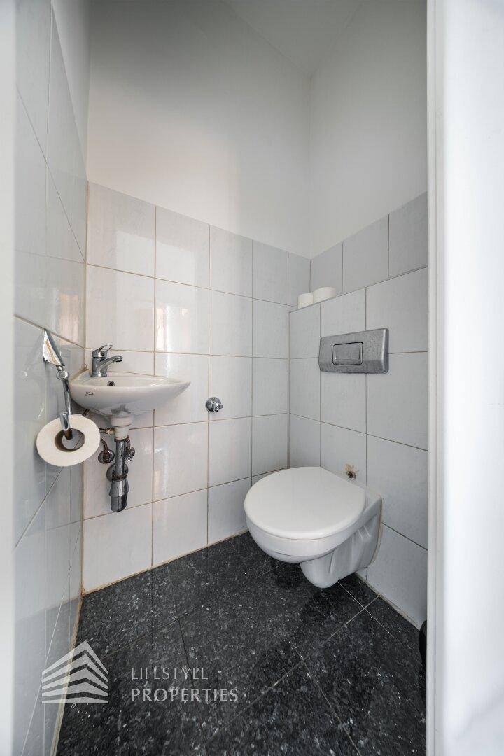 Kleines Gäste-WC mit Wand-WC, Waschbecken und hellen Fliesen an den Wänden.