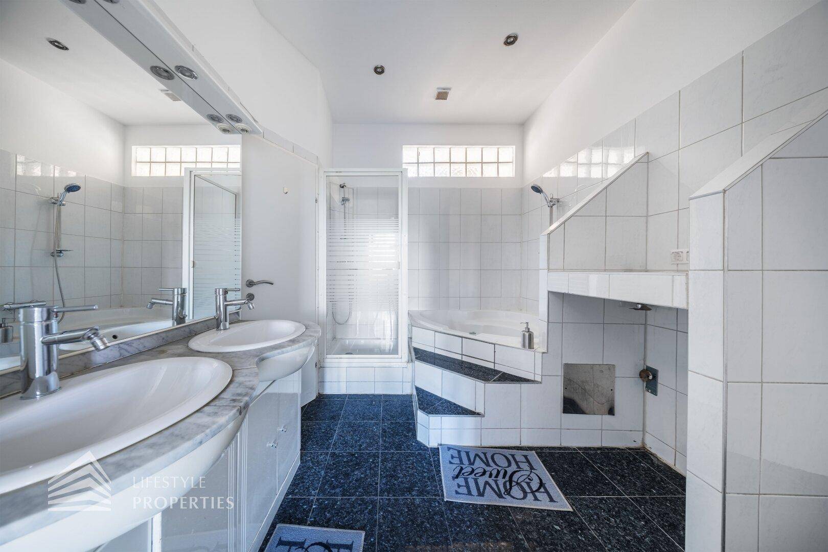 Geräumiges Badezimmer mit Doppelwaschbecken, Dusche und einer erhöhten Badewanne.