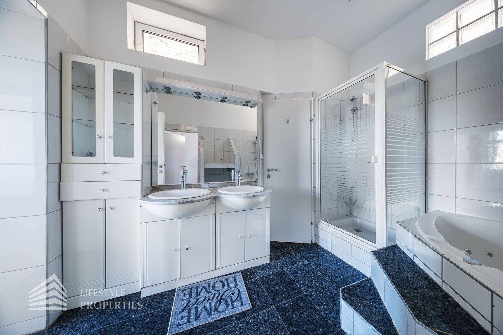 Helles Badezimmer mit Doppelwaschbecken, Duschkabine und einer erhöhten Badewanne.