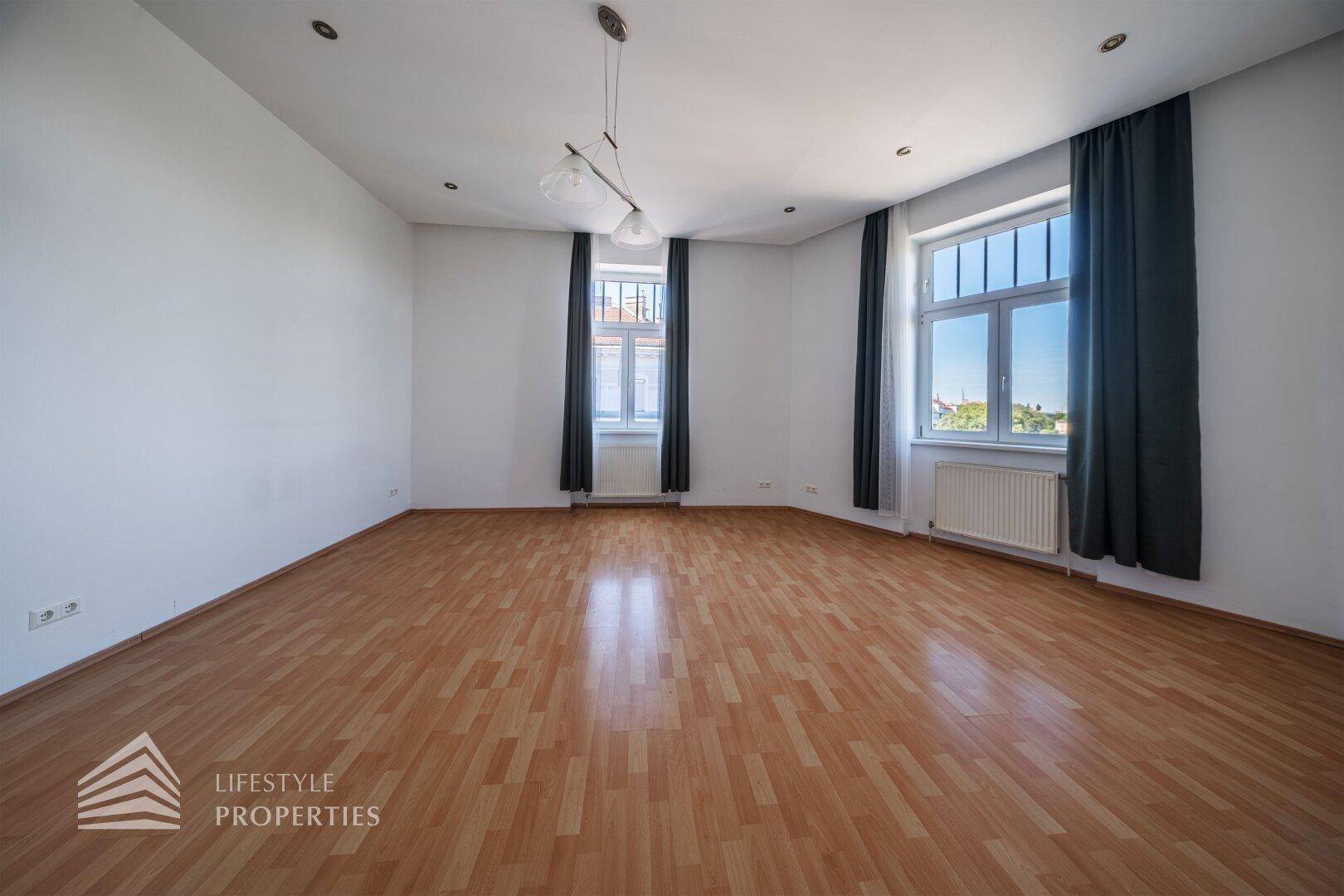 Helles Zimmer mit Parkettboden und zwei Fenstern, die viel natürliches Licht hereinlassen.