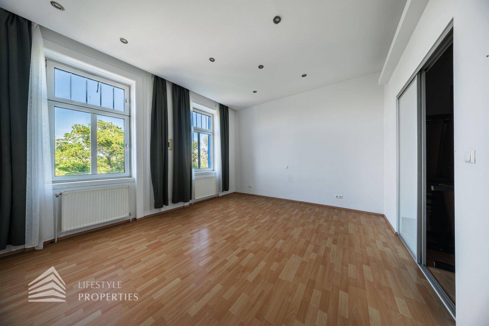 Geräumiges Zimmer mit Parkettboden, großen Fenstern und integriertem Schrankbereich.