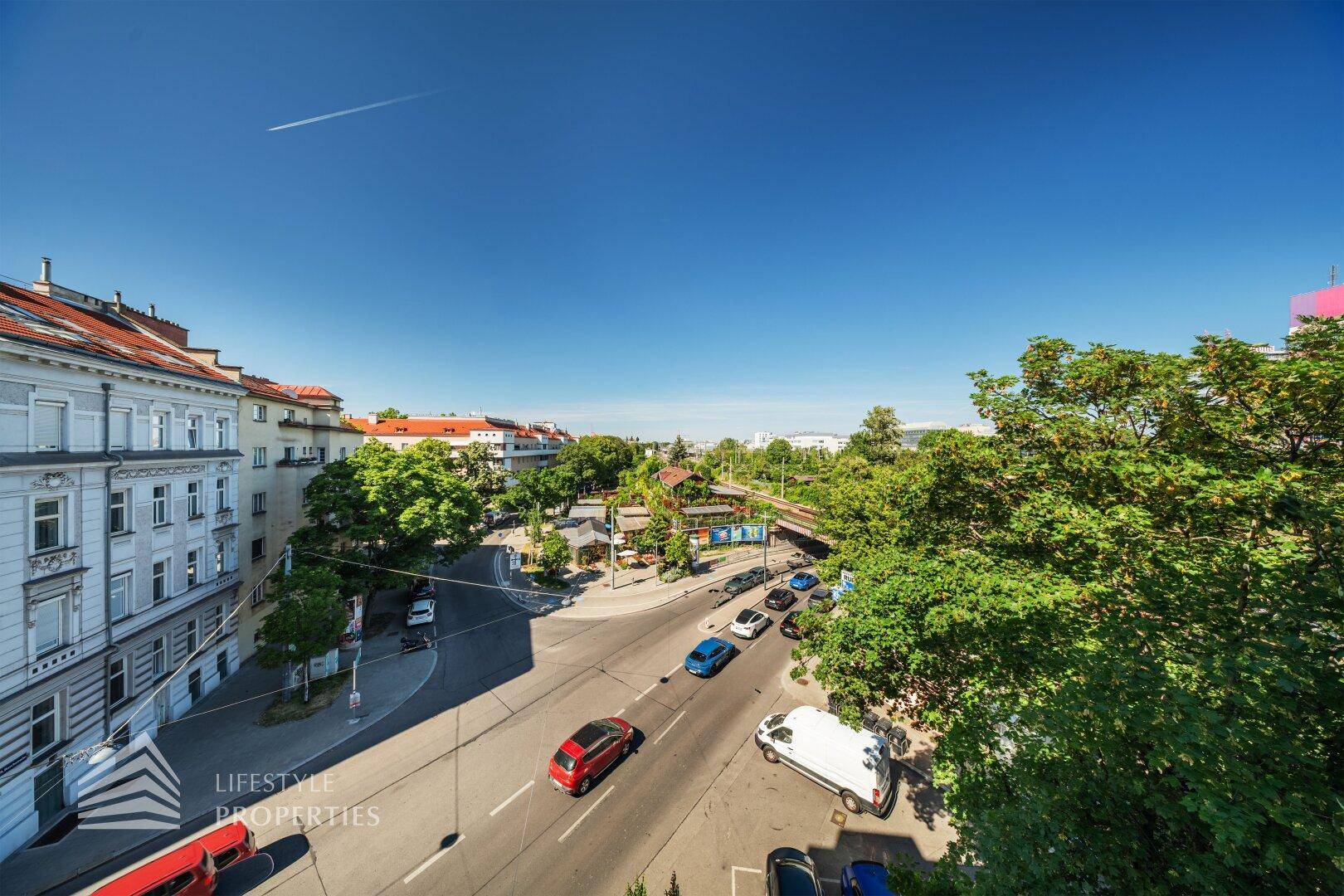 Weitläufiger Blick über eine belebte Straße mit Gebäuden und viel Grün.