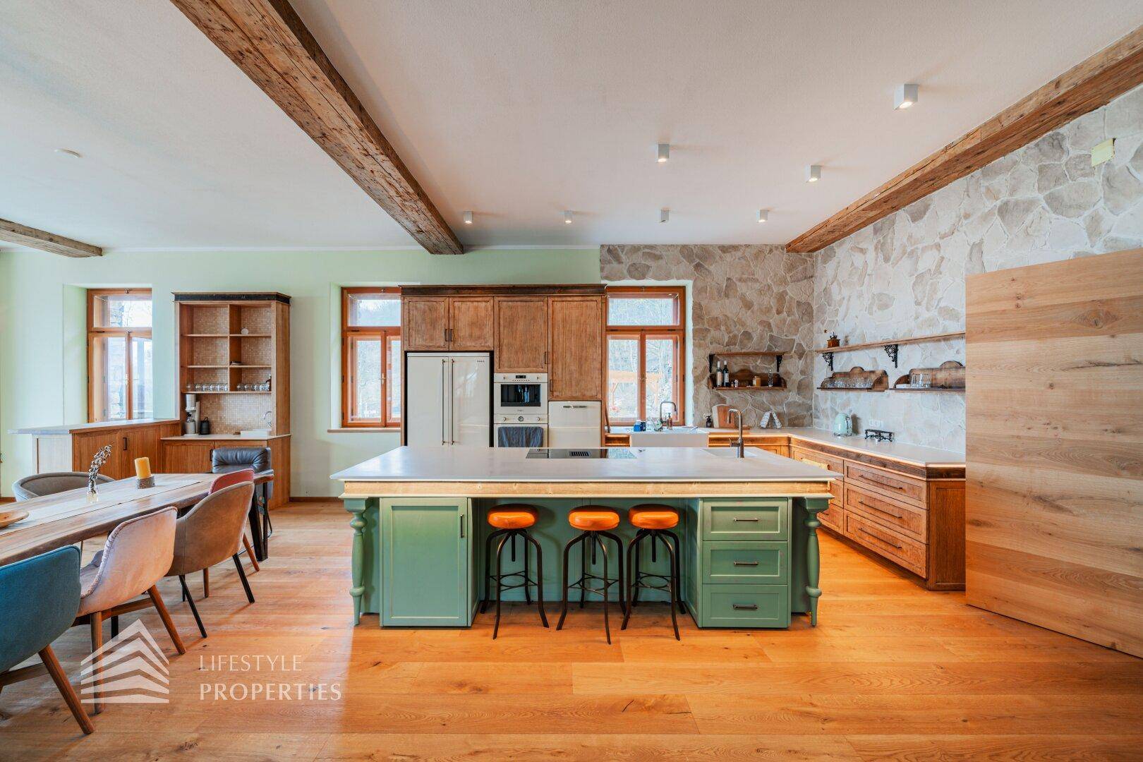 Moderne Küche mit grüner Insel, Holzelementen und Steinwand, offen zum Essbereich.