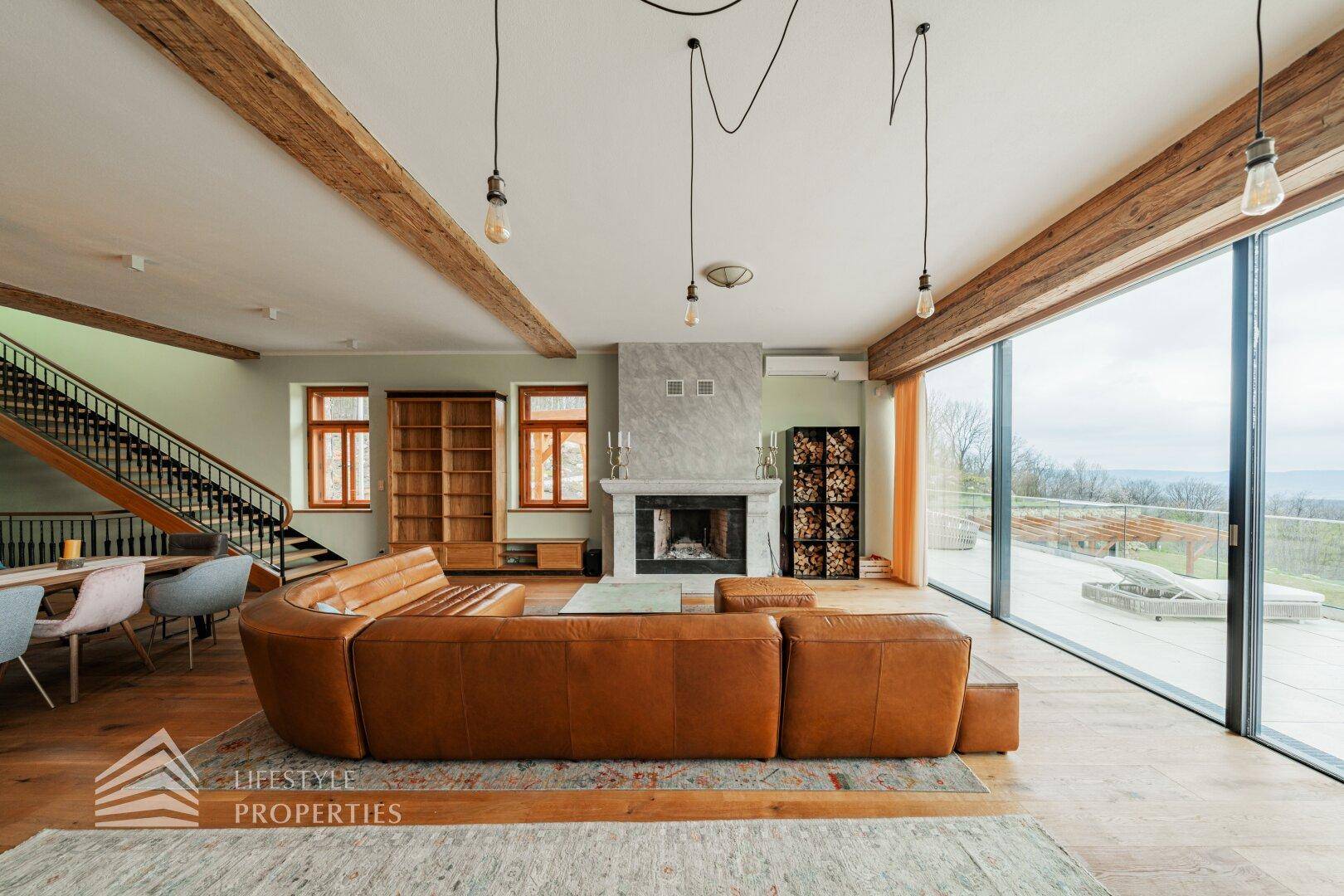 Geräumiger Wohnbereich mit Ledersofa, Kamin und Treppe, offen zur Küche mit Panoramafenstern.