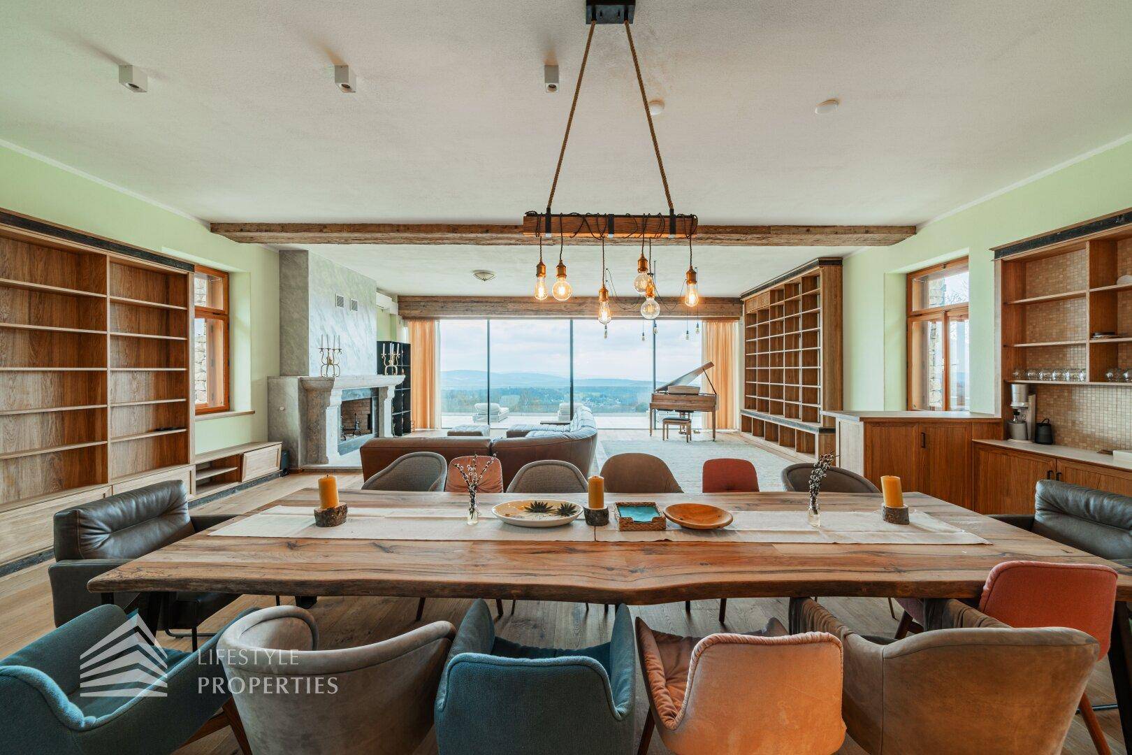 Großer Essbereich mit Holztisch und Blick auf den Wohnbereich mit Flügel und Panoramafenstern.