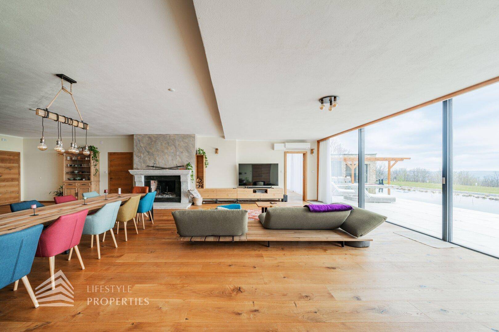 Heller Wohnbereich mit Ledersofa, Kamin und raumhohen Fenstern, die einen weiten Blick bieten.