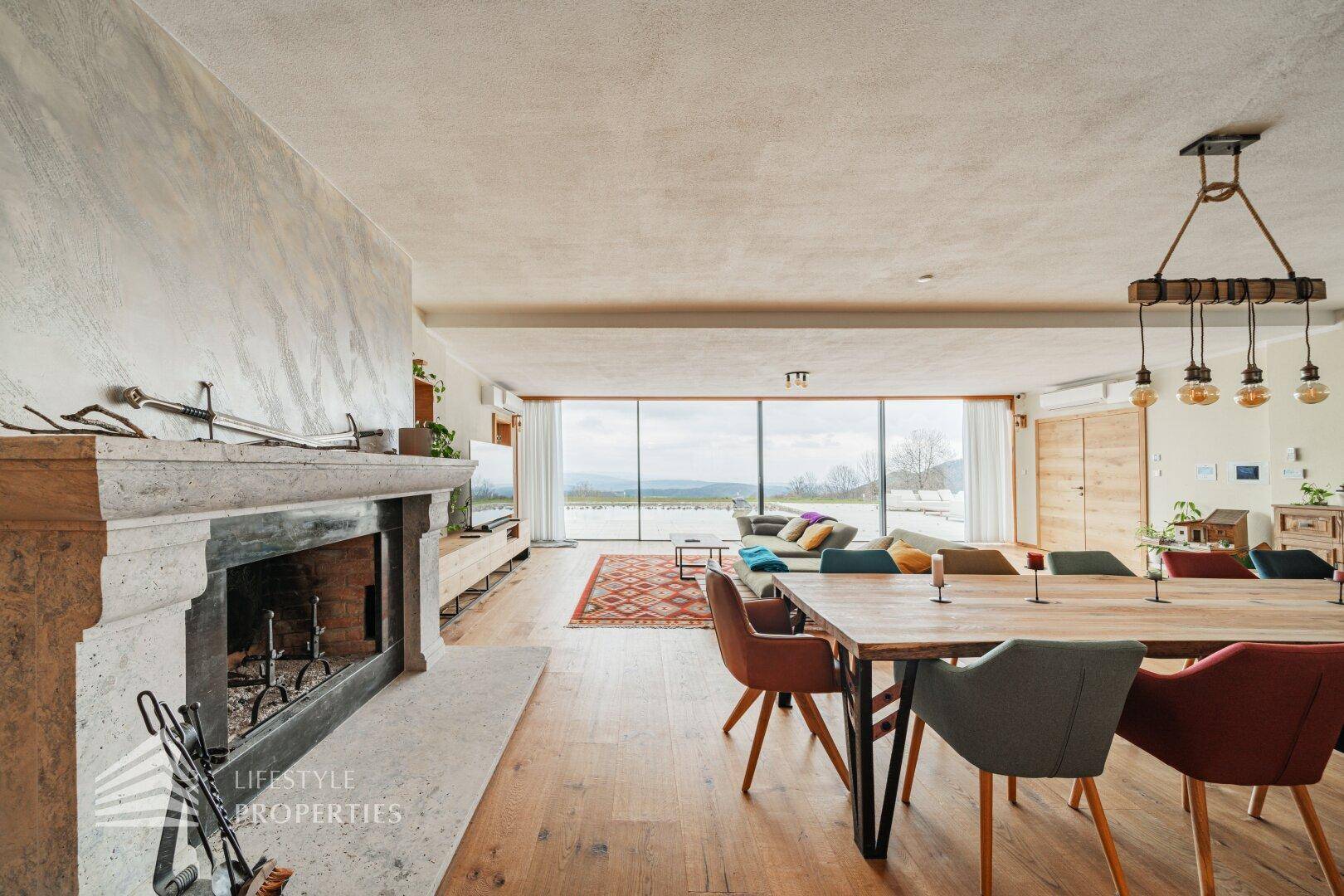 Heller Wohn- und Essbereich mit Kamin, Holzboden und raumhohen Fenstern mit Weitblick.