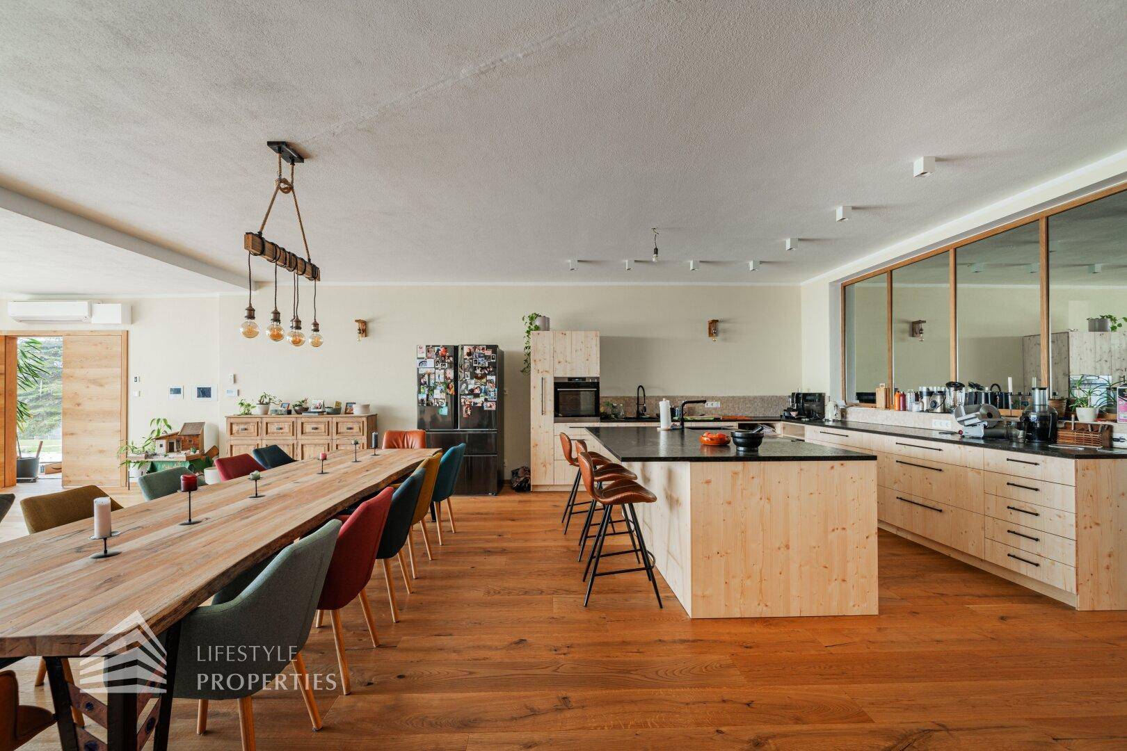 Offener Wohn- und Essbereich mit Holzboden, langer Tafel und moderner Küche mit Insel.