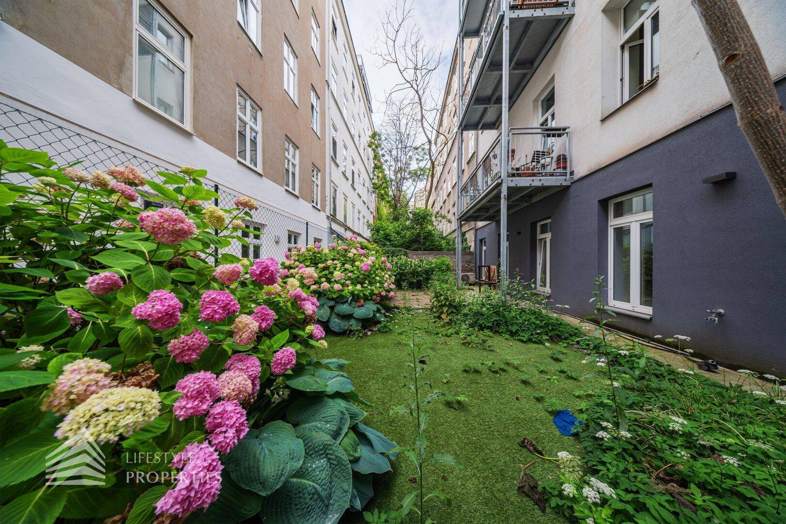 Grüner Innenhofgarten mit blühenden Hortensien und Blick auf die umliegenden Gebäude.